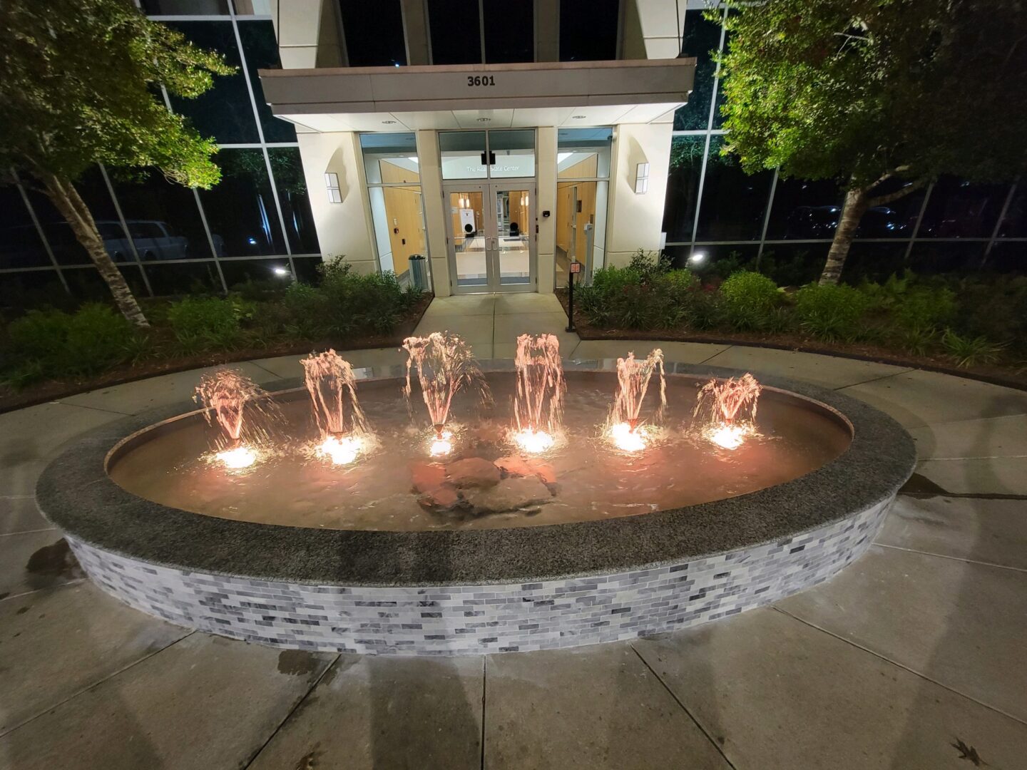 Illuminated circular fountain outside office building entrance