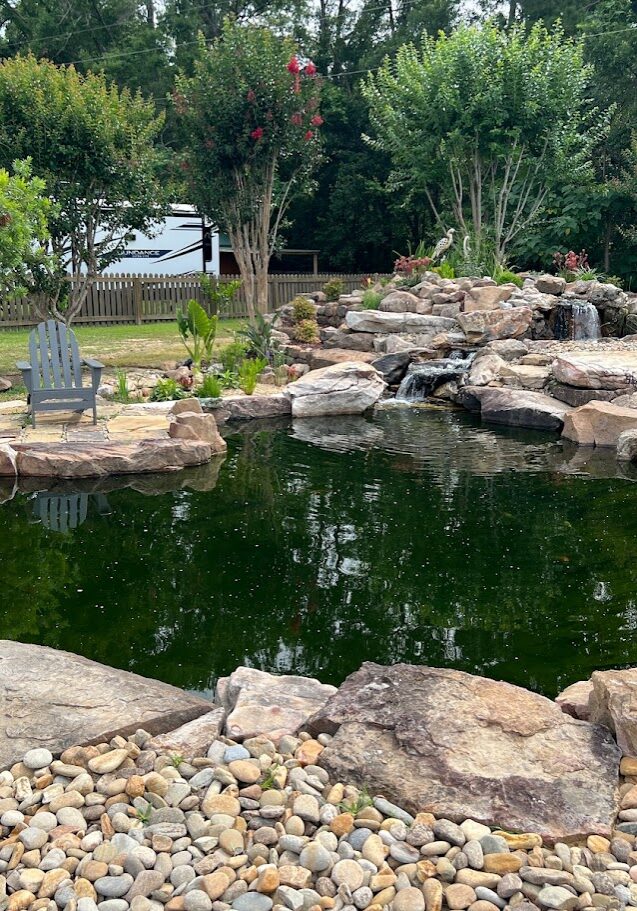 Rock-lined backyard pond with waterfall and chairs